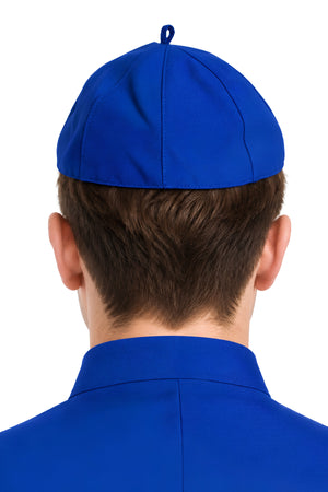 Back view of a person wearing a royal blue eight-panel zucchetto clergy skullcap, showing its fitted shape, stitched seams, and crown loop.