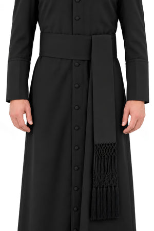 Black Steadfast Devotion band cincture worn over a clergy cassock, featuring a wide waist band and long hand-knotted fringe ends.