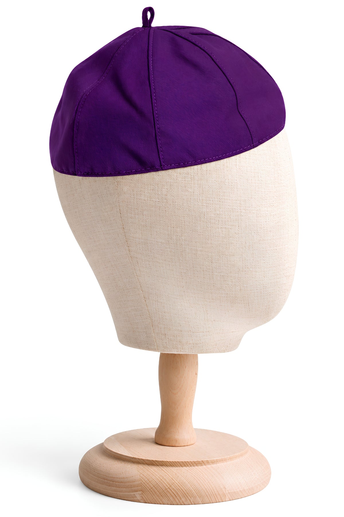 Roman purple eight-panel clergy zucchetto skullcap displayed on a beige linen head mannequin with a wooden stand, featuring stitched panel seams and a small crown loop.
